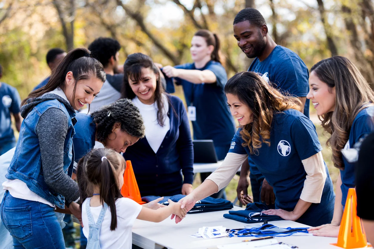 Mid adult volunteer shakes hands with girl at registration table stock photo