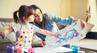 An adult teaching a primary school child to paint at home