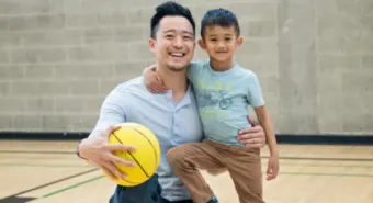 happy parent and child posing with a basketball on an indoor basketball court