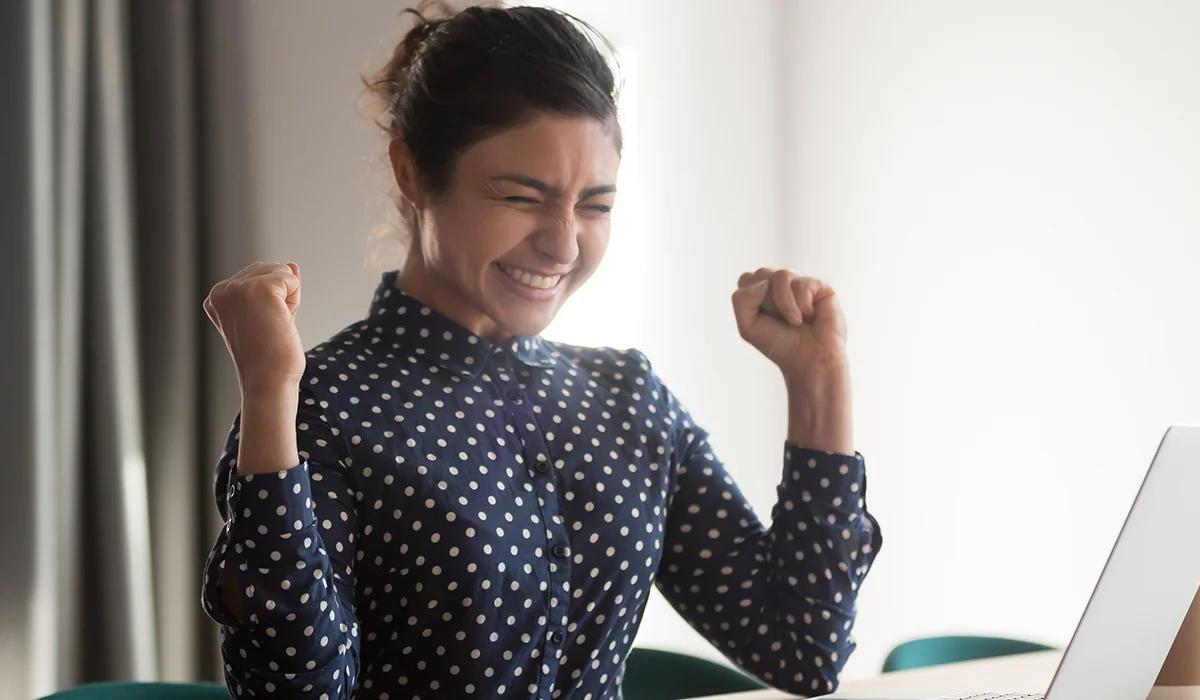a woman pumping her fists in success in front of a computer